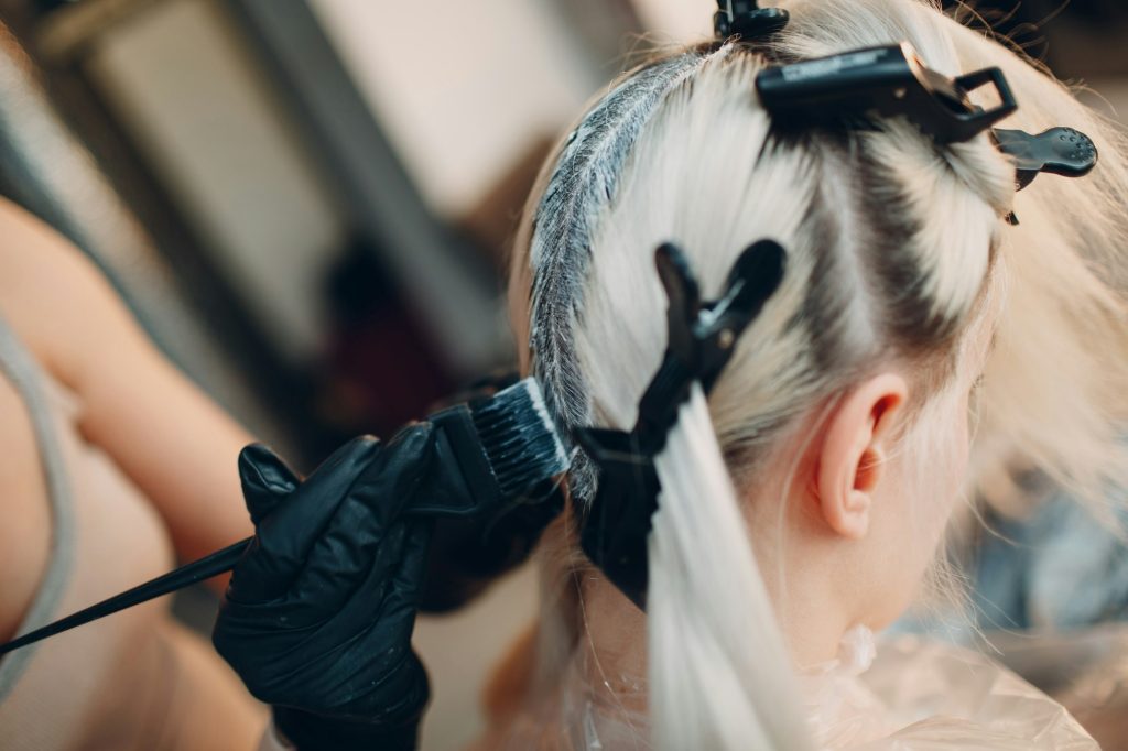 Young woman hairdresser dying hair at beauty salon. Professional hair roots coloring